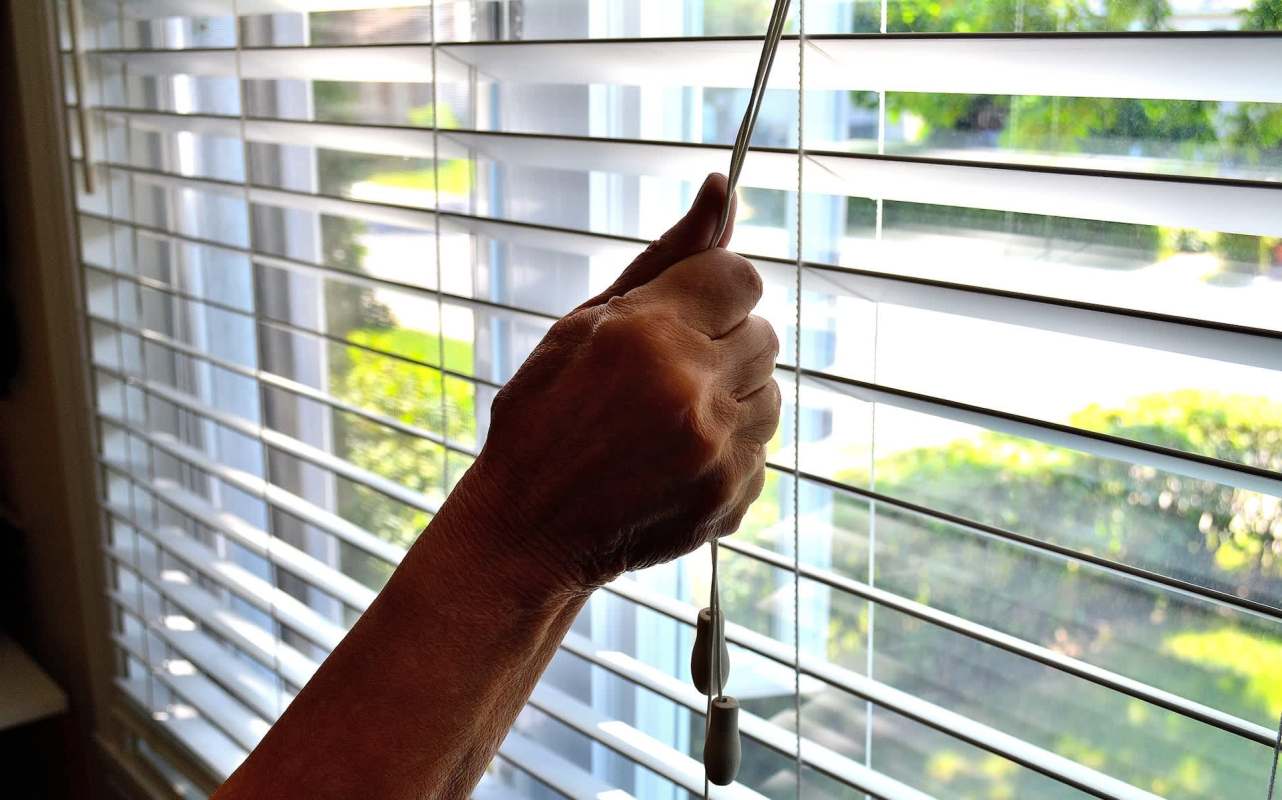 A hand adjusting the cord of horizontal blinds.