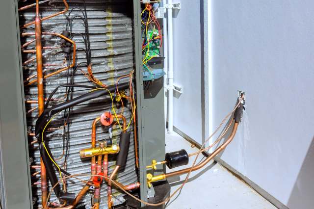 An open electrical panel showing copper tubing and wiring inside an air conditioning unit.