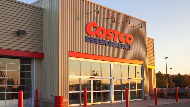 The exterior of a Costco Wholesale warehouse with large windows and red accents at sunset.
