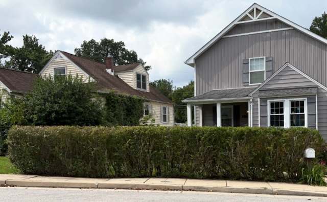 Two adjacent houses with different architectural styles, separated by a neatly trimmed hedge.