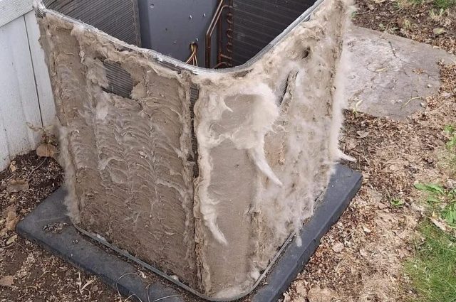 A dusty air conditioning unit disassembled on the ground, surrounded by grass and dirt.