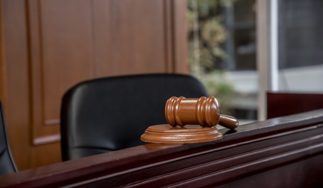 A wooden gavel rests on a desk in a courtroom with leather chairs and a blurred background.