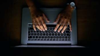A person's hands typing on a laptop keyboard in a dimly lit environment.