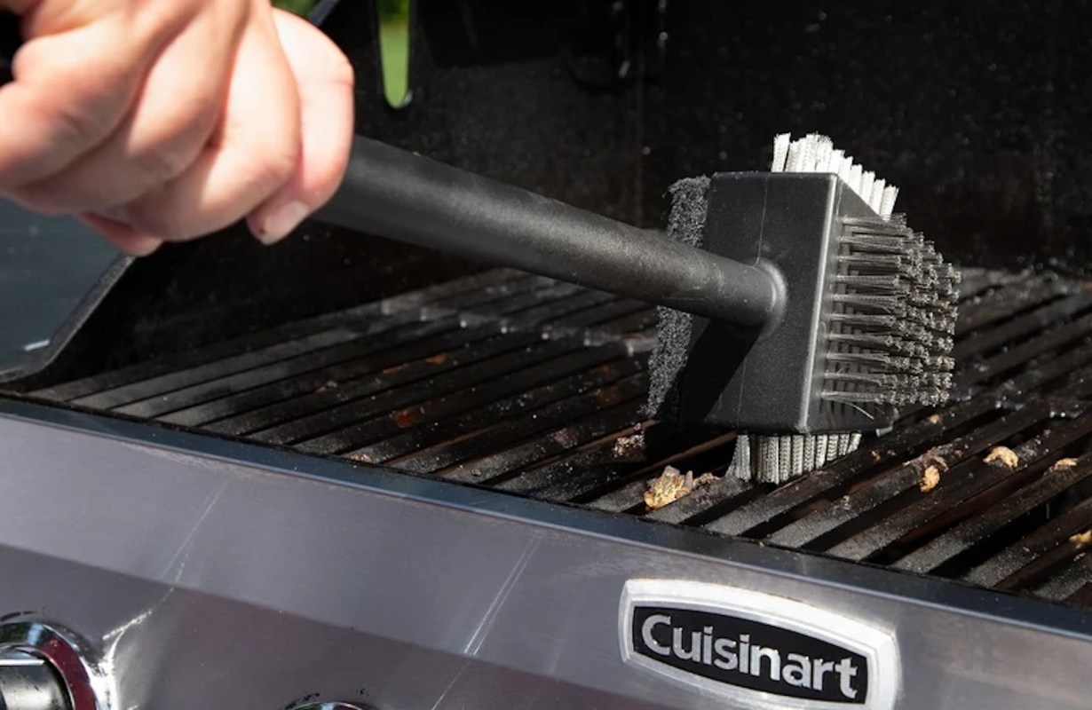 A person cleaning a grill with a brush.