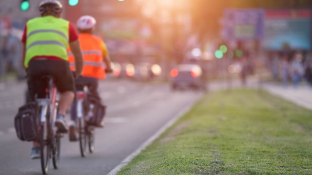 Two cyclists in reflective vests ride along a busy street during sunset.