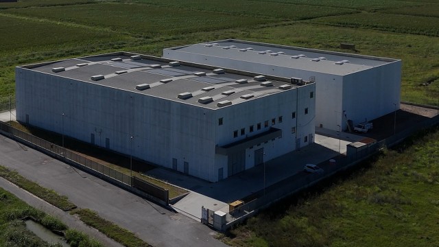 An aerial view of two large, white industrial buildings surrounded by green fields.
