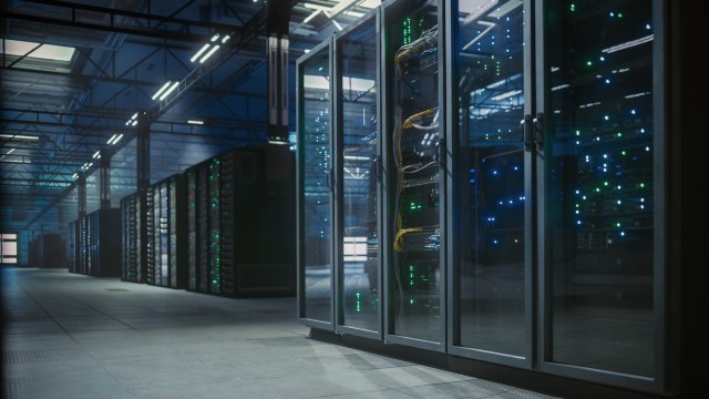 A data center aisle lined with server racks, illuminated by green and blue lights.