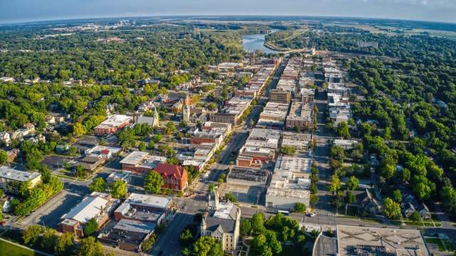 Aerial view of a vibrant town with tree-lined streets, historic buildings, and a river in the background.