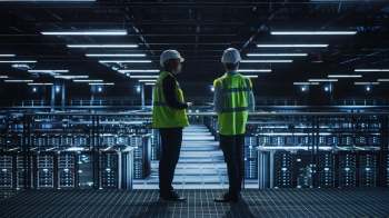 Two workers in safety gear inside a data center.