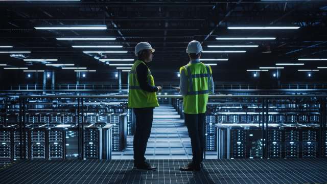 Two workers in safety gear inside a data center.