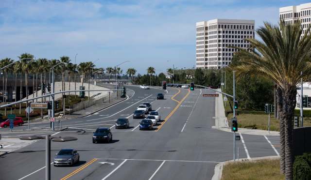 A busy intersection with cars, palm trees, and tall buildings under a clear blue sky.