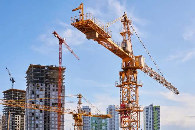 Construction cranes are positioned near multi-story buildings under construction against a blue sky.