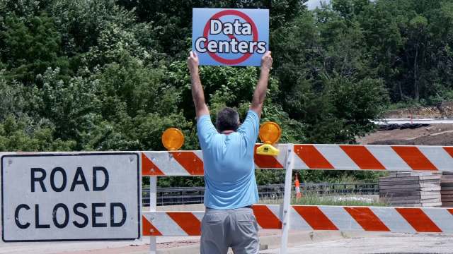 A person holding a sign that says "Data Centers" in front of a road closed barrier with construction in the background.