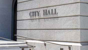 The words "CITY HALL" are engraved on a stone wall next to a set of stairs and a handrail.