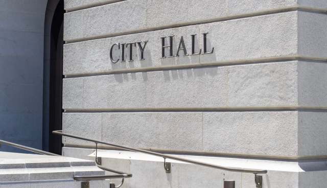 The words "CITY HALL" are engraved on a stone wall next to a set of stairs and a handrail.