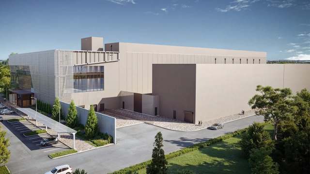 A modern industrial building with large windows and a landscaped parking area under a clear blue sky.