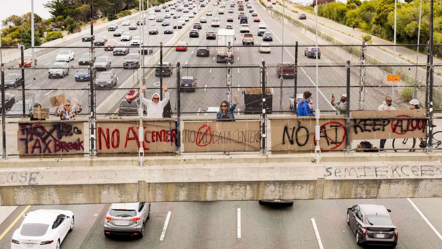Protesters holding anti-data center signs on a highway overpass.