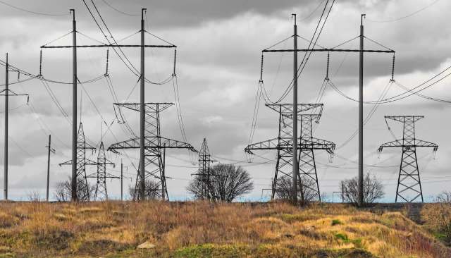 A landscape featuring tall electricity pylons silhouetted against a cloudy sky and sparse vegetation.