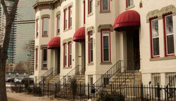 A row of historic apartment buildings with red awnings and steps, set against a backdrop of modern skyscrapers.