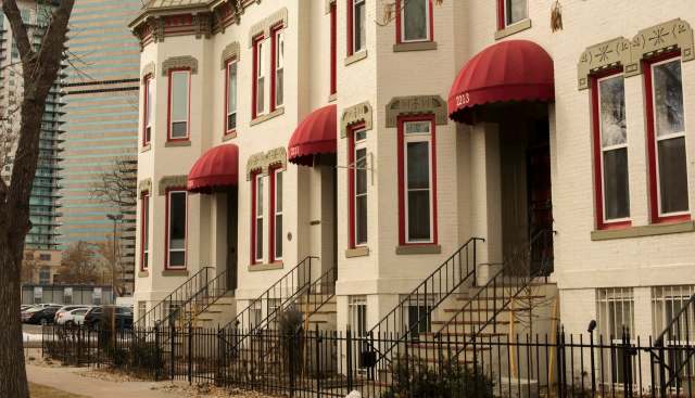 A row of historic apartment buildings with red awnings and steps, set against a backdrop of modern skyscrapers.