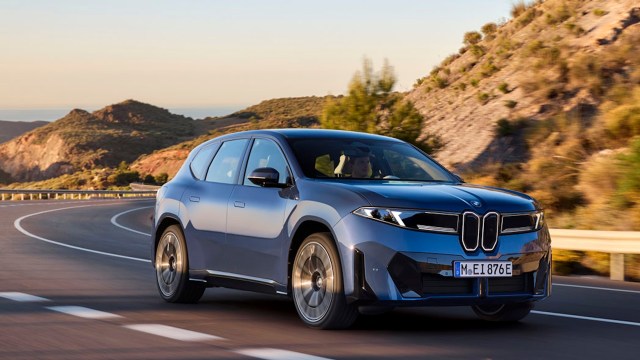 A blue BMW SUV drives along a winding road with mountainous scenery in the background.