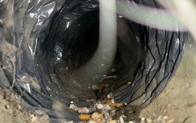 A close-up view of a dark, cylindrical tunnel lined with black material and debris at the bottom.