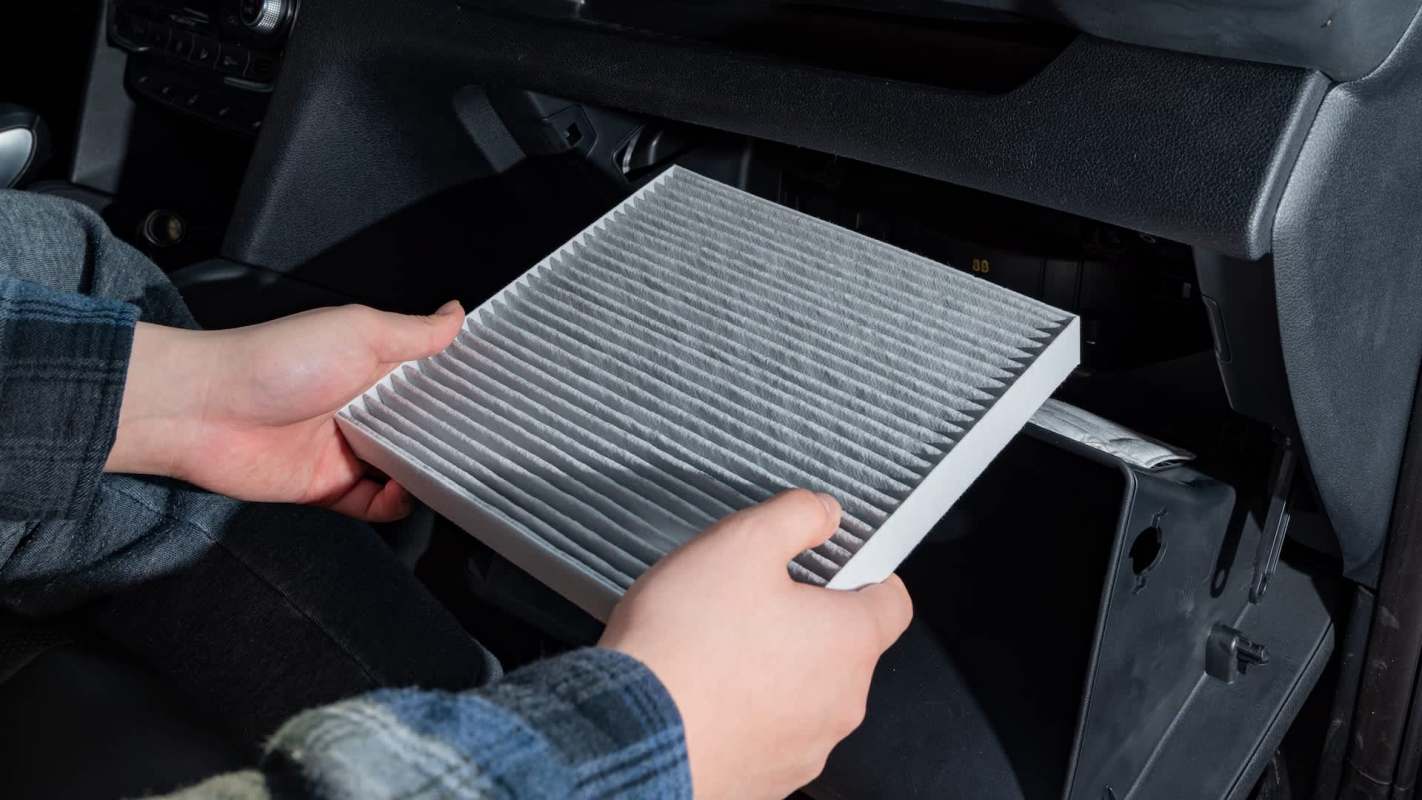A person holds a car air filter while accessing the glove compartment of a vehicle.