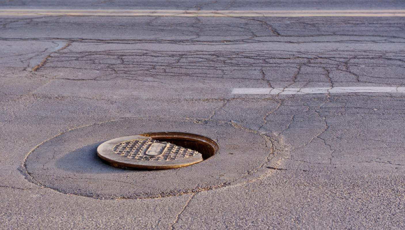 A partially open manhole cover on a cracked asphalt road.
