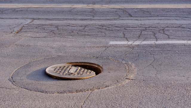 A partially open manhole cover on a cracked asphalt road.