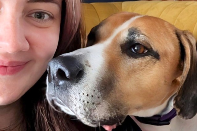 A woman smiles while posing closely with a dog on a yellow couch.