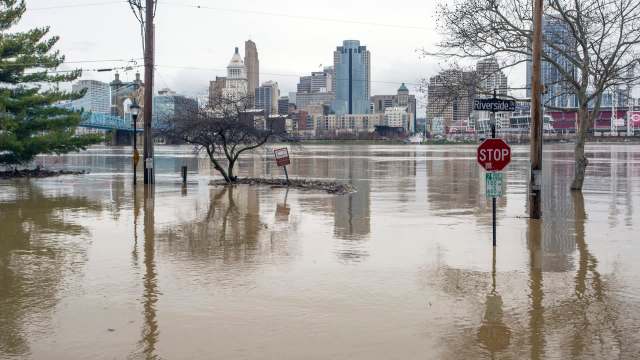 The Cincinnati city skyline partially submerged in floodwaters with trees and street signs visible above the water.