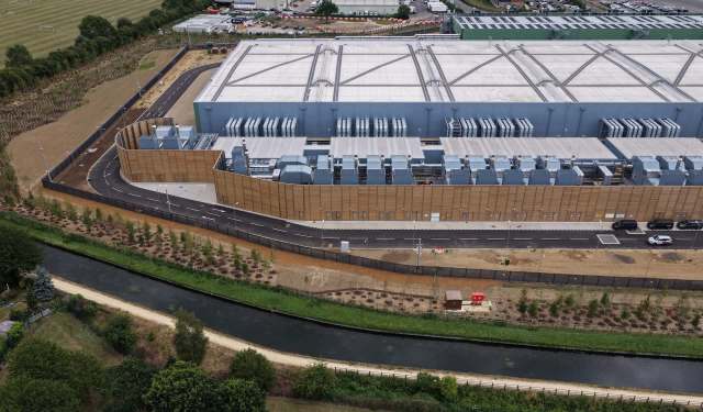 Aerial view of an industrial facility with cooling units, surrounded by a road and a waterway lined with trees.