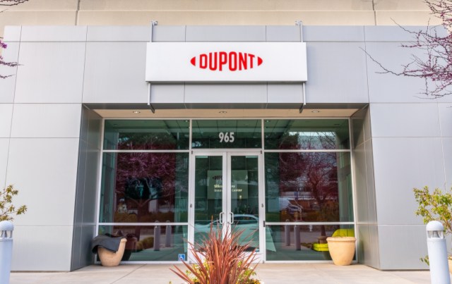 The entrance of a modern building featuring a "DUPONT" sign and large glass doors, surrounded by landscaping.