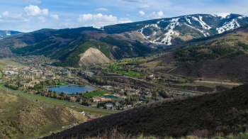 A panoramic view of a mountainous landscape with a valley, a lake, and a small town below under a blue sky.