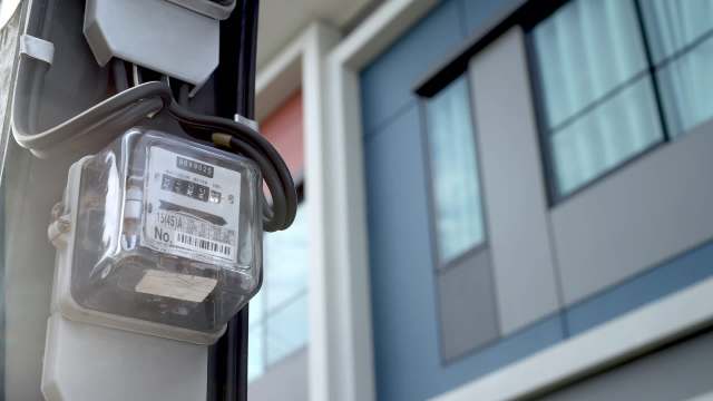 An electric meter attached to a building with modern architecture in the background.