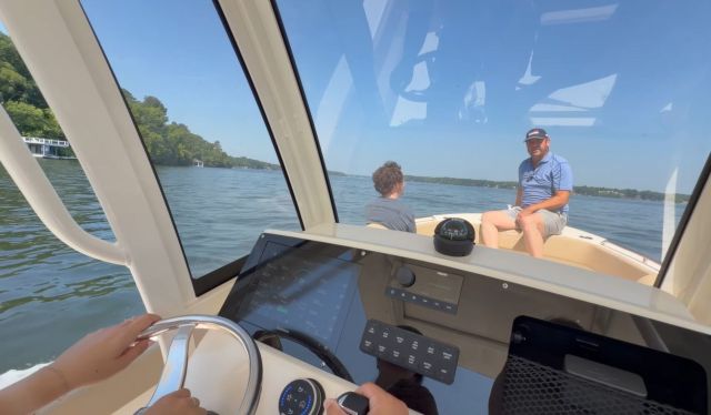 Two people sitting on an electric boat as a third person steers.