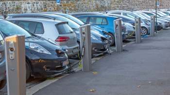 Several electric vehicles are parked beside charging stations in an outdoor parking lot.