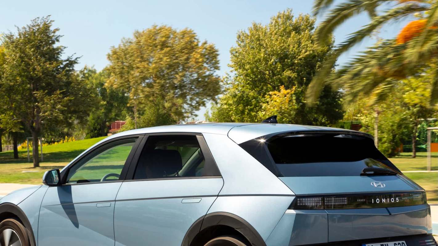 A blue Hyundai Ioniq 5 electric vehicle parked in a sunny park with trees in the background.