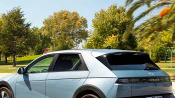 A blue Hyundai Ioniq 5 electric vehicle parked in a sunny park with trees in the background.