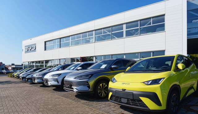A lineup of various BYD electric vehicles displayed outside a modern dealership under a clear blue sky.