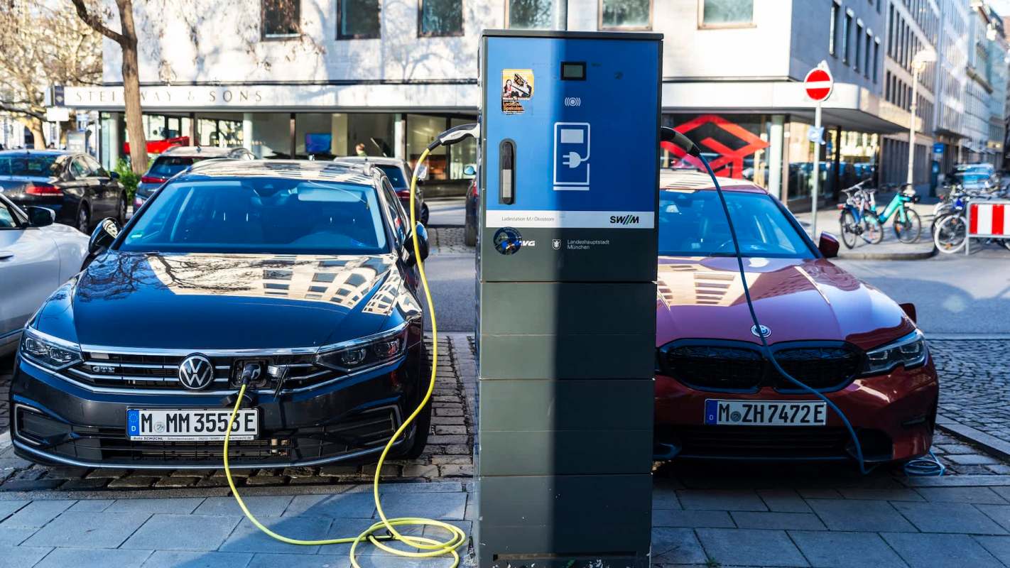 Two electric cars, a black Volkswagen and a red BMW, are parked beside an electric charging station.