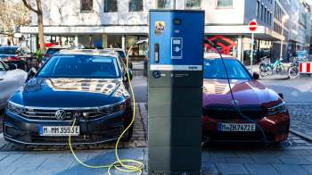 Two electric cars, a black Volkswagen and a red BMW, are parked beside an electric charging station.