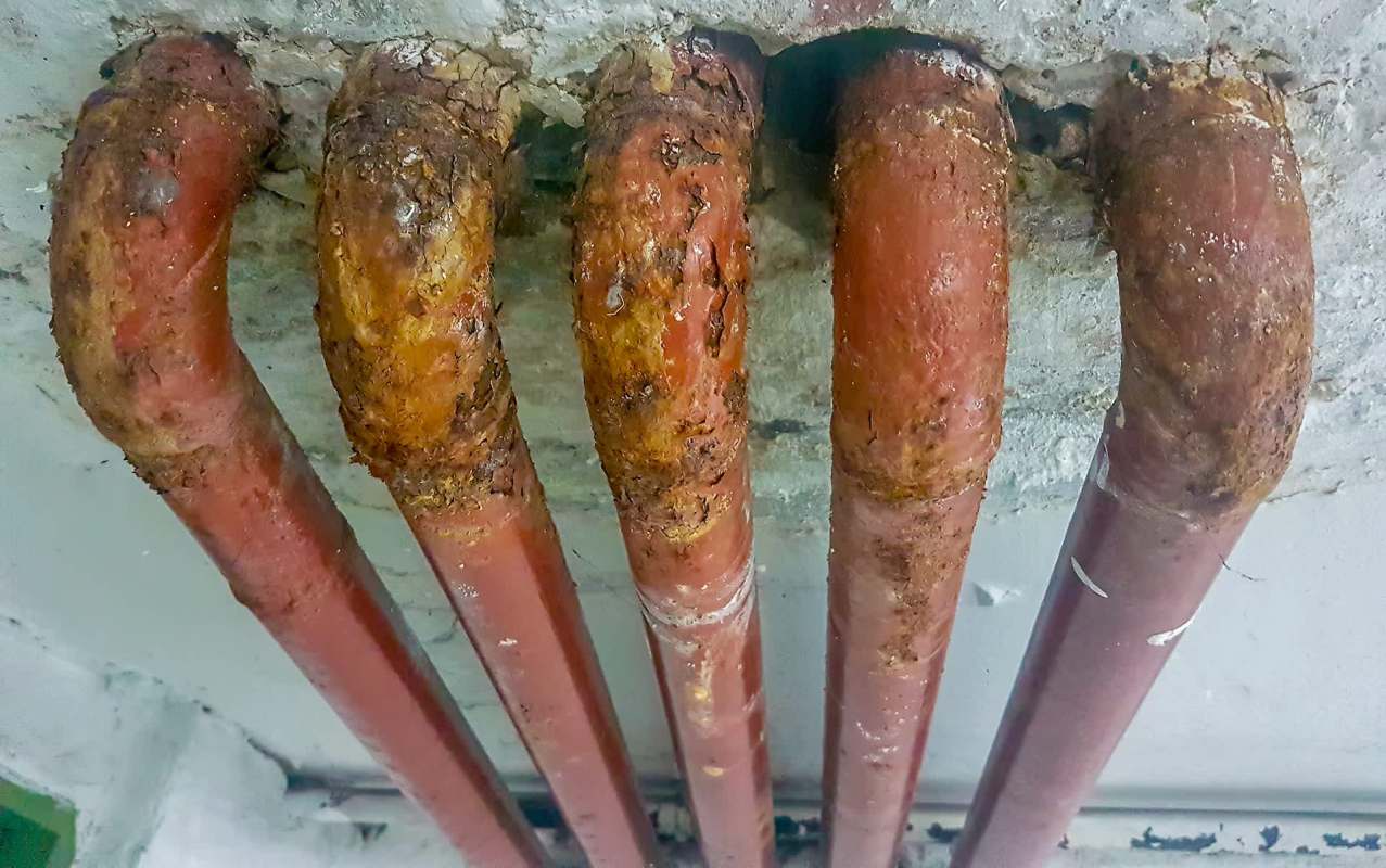 A close-up of rusted and deteriorating red pipes attached to a ceiling.