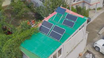 A green corrugated roof with solar panels on mounts.