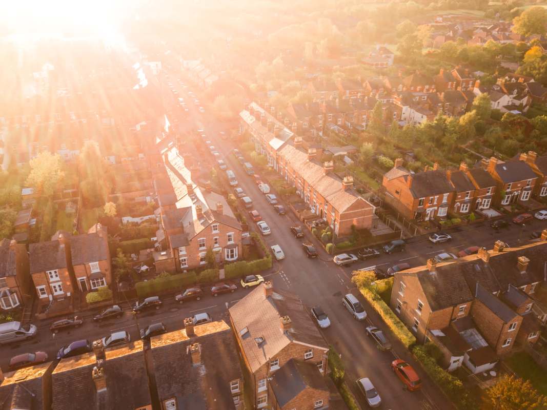An aerial view of suburban streets lined with houses and parked cars during golden hour light.