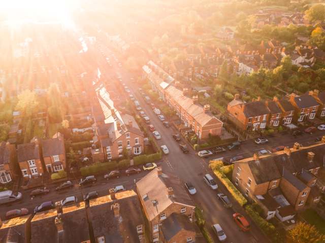 An aerial view of suburban streets lined with houses and parked cars during golden hour light.