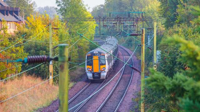 A train rounds a curve on a track surrounded by trees and electric poles.