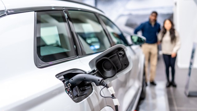 Two people looking at an electric vehicle plugged into a charger.