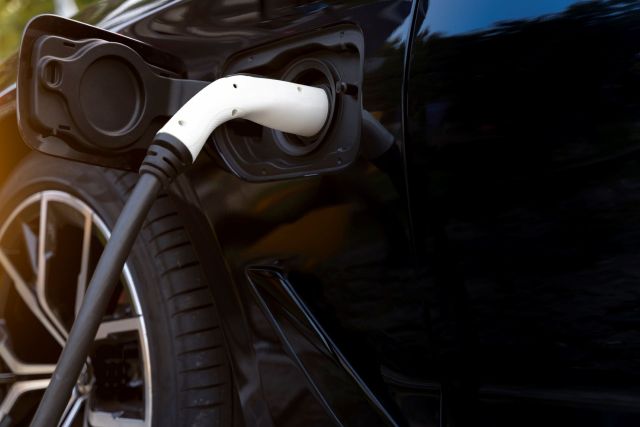 An electric vehicle charging cable plugged into the port of a black car.