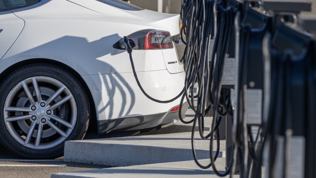 A white electric car is charging at a station with multiple charging cables.